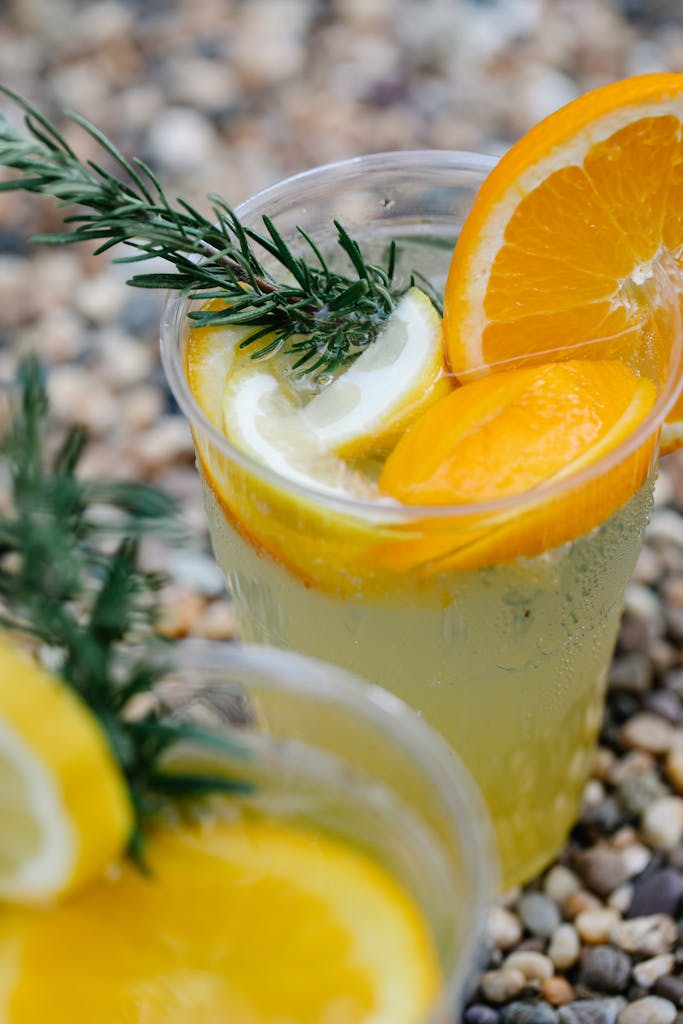 Close-up of citrus lemonade in a cup with oranges, lemons, and mint on pebble background.