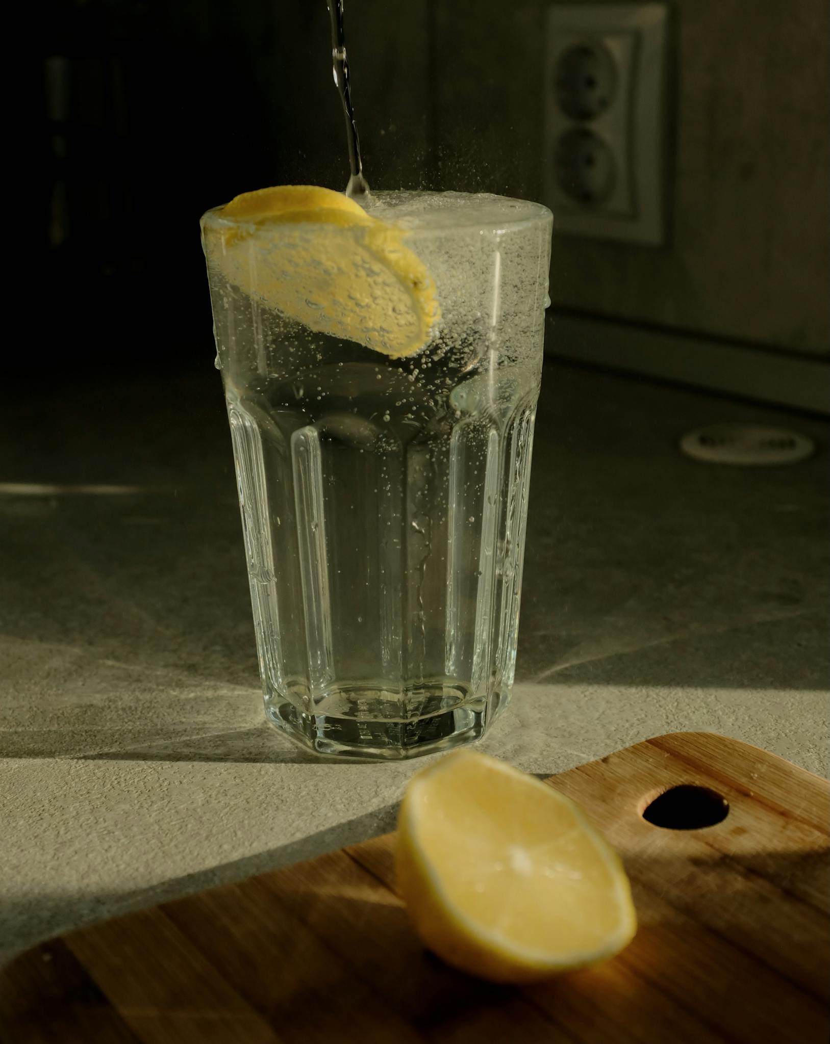Fresh lemon slice splashes into a glass of water on a kitchen counter.