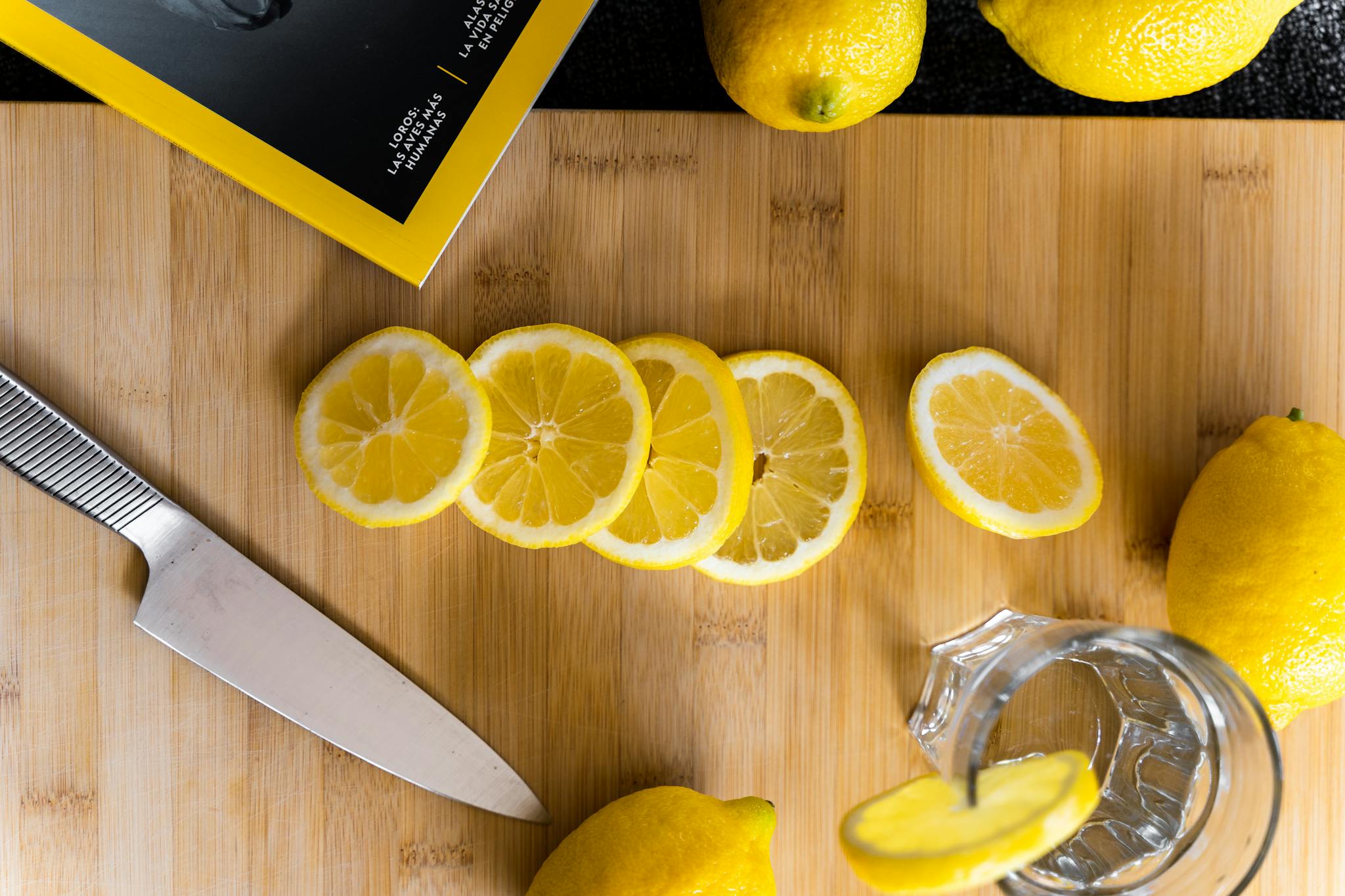 Overhead view of sliced lemons and knife on a wooden board, perfect for refreshing lemonade or culinary use.